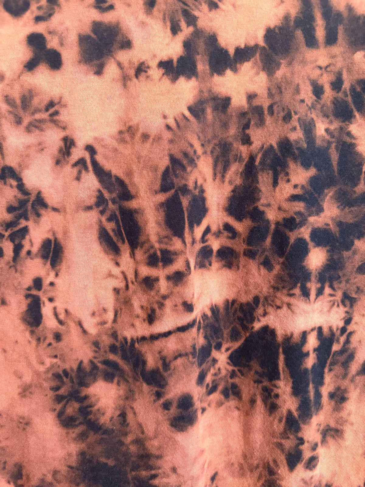 Close up detail of rust orange and black bleach crumple tie dye pattern texture on cotton shirt