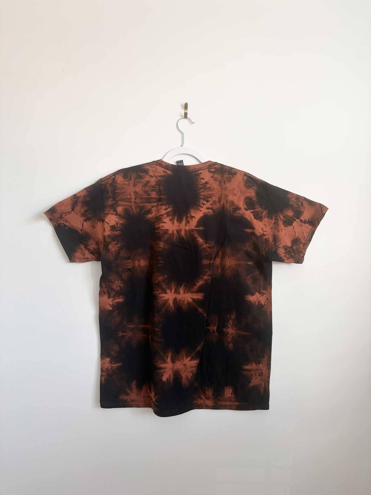 Back view of black and rust orange shibori bleach tie dye t-shirt hanging on white hanger