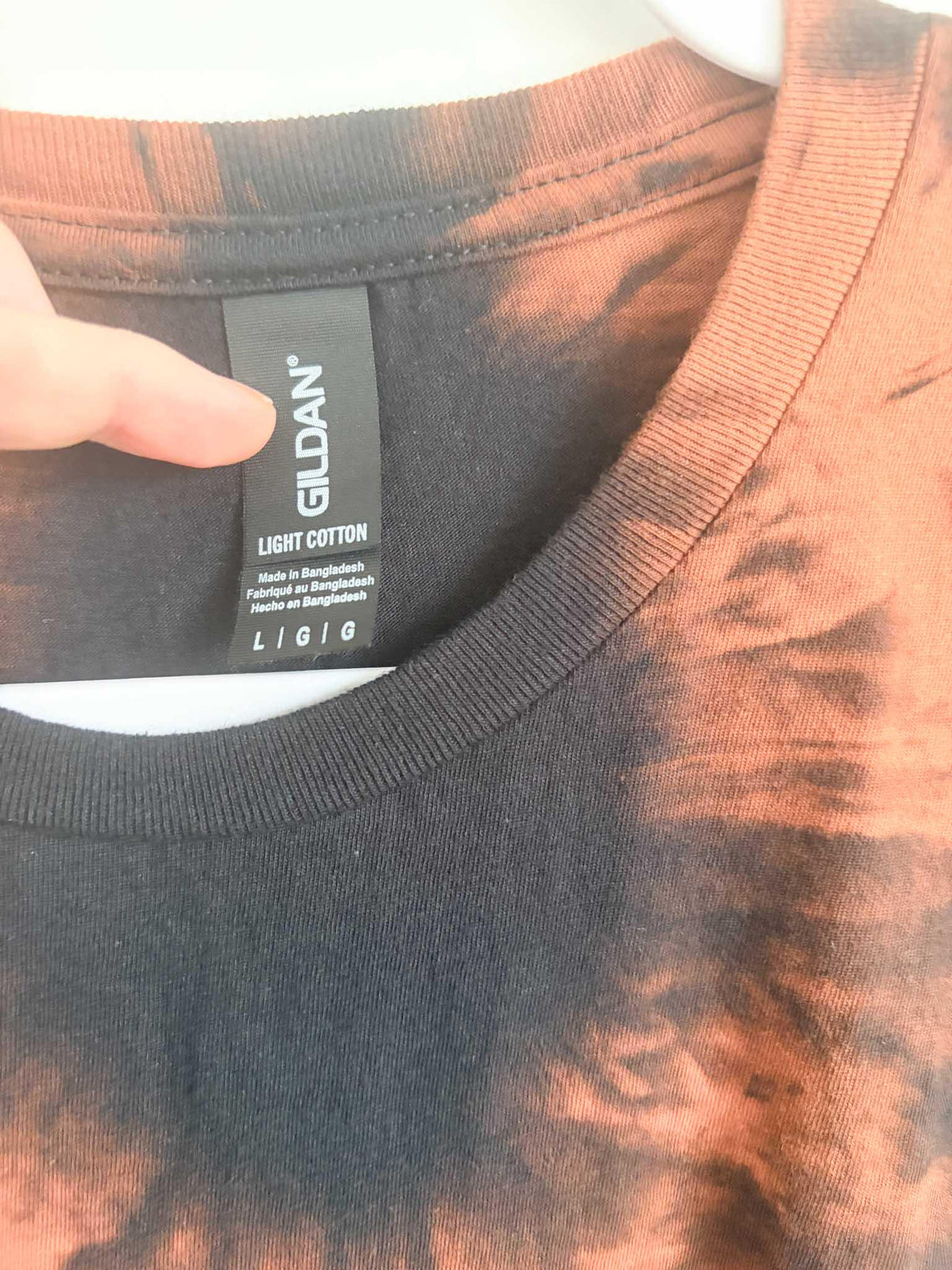 Close up of Gildan Light Cotton size large tag on black and rust orange shibori bleach tie dye shirt