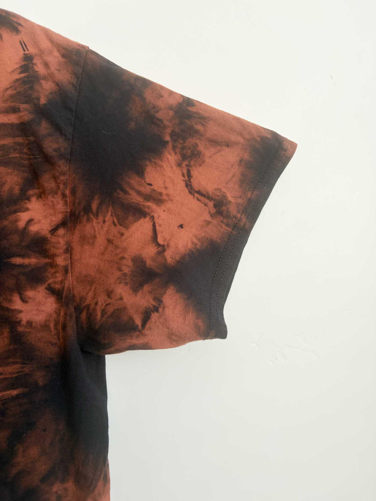 Close up of sleeve and side seam on black and rust orange shibori bleach tie dye t-shirt