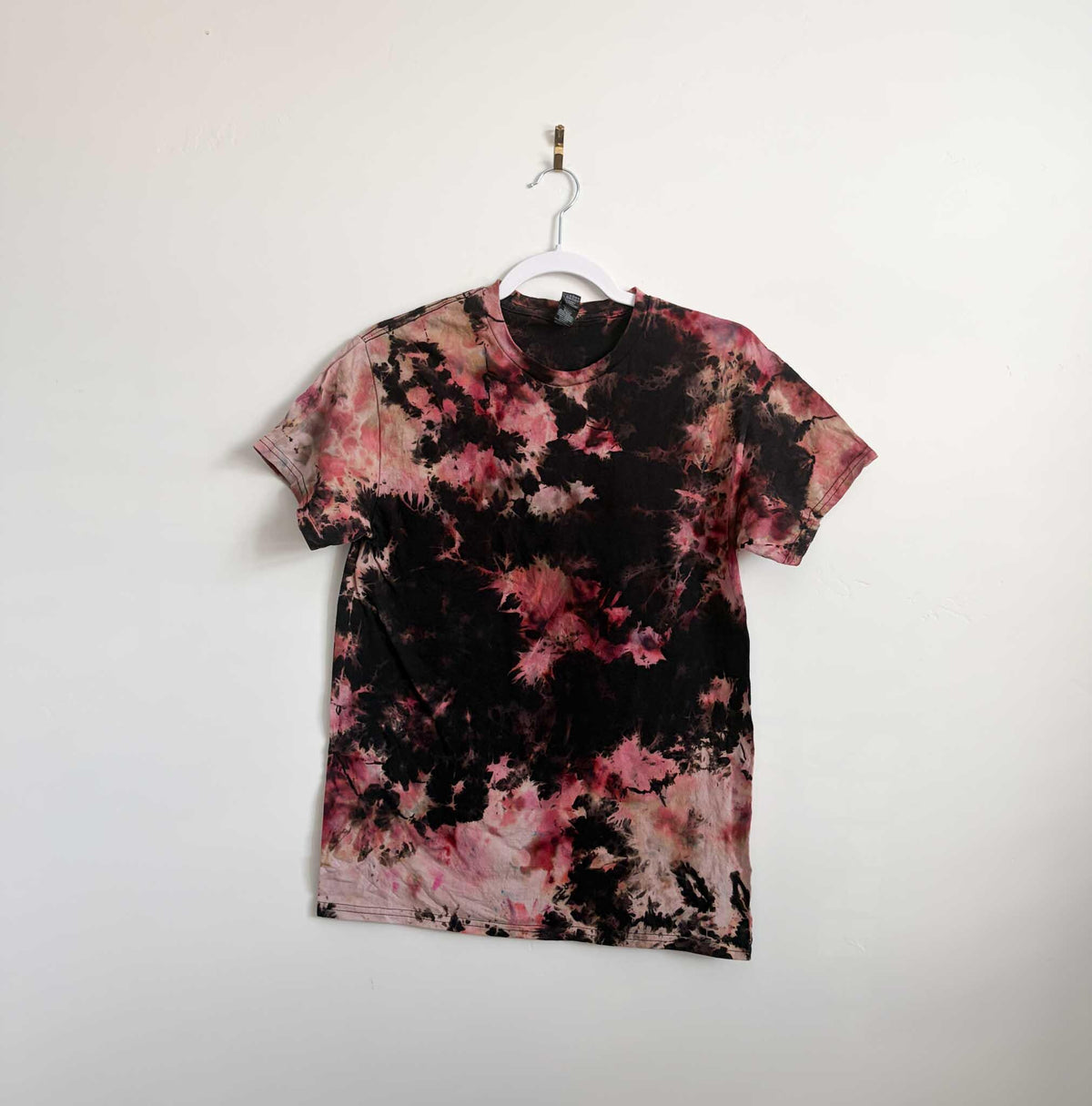 Small black red and pink blood moon bleach crumple tie dye t-shirt hanging on white hanger against white wall