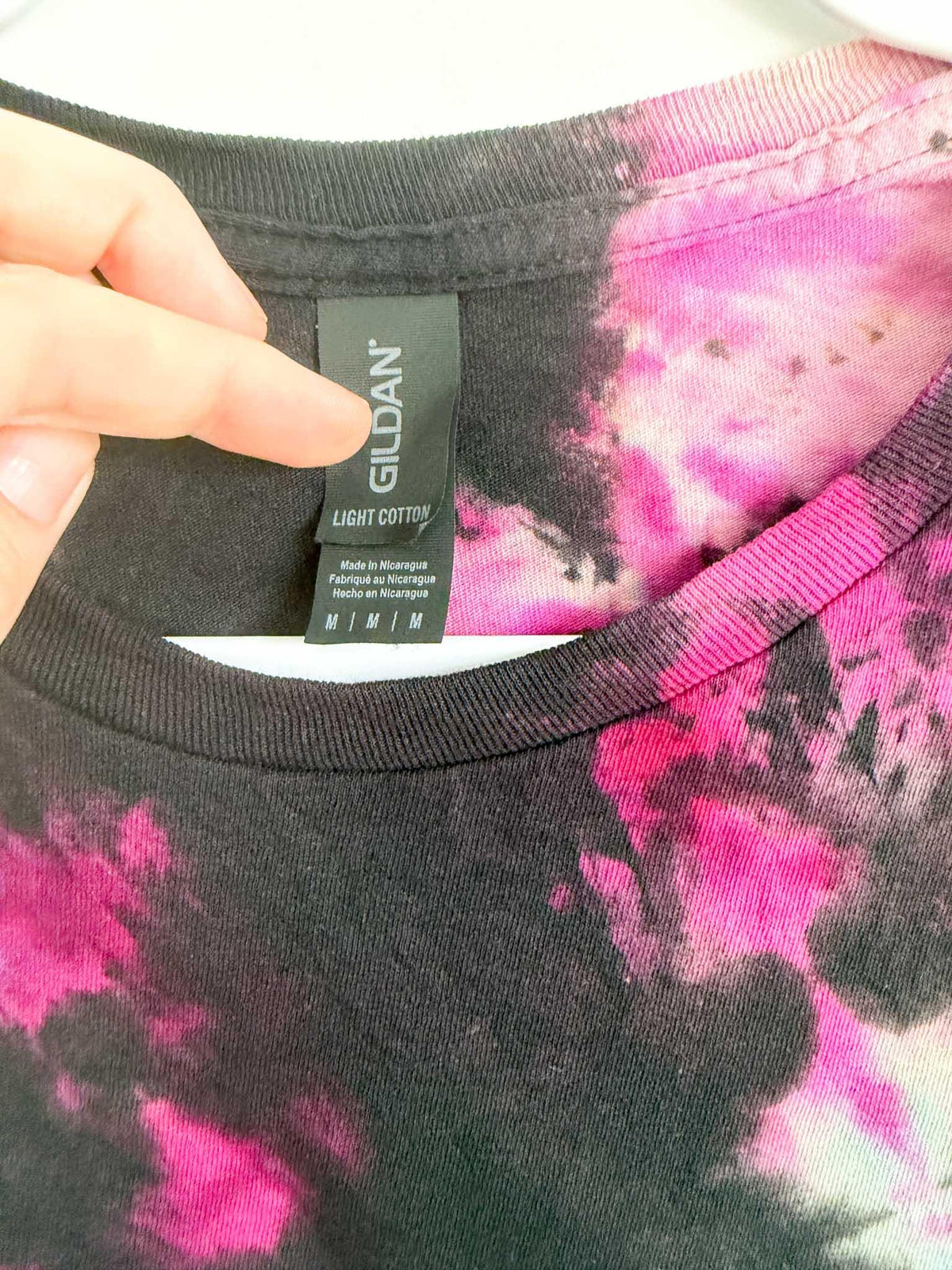 Close up of Gildan Light Cotton size medium tag on black pink and purple galaxy spiral tie dye shirt