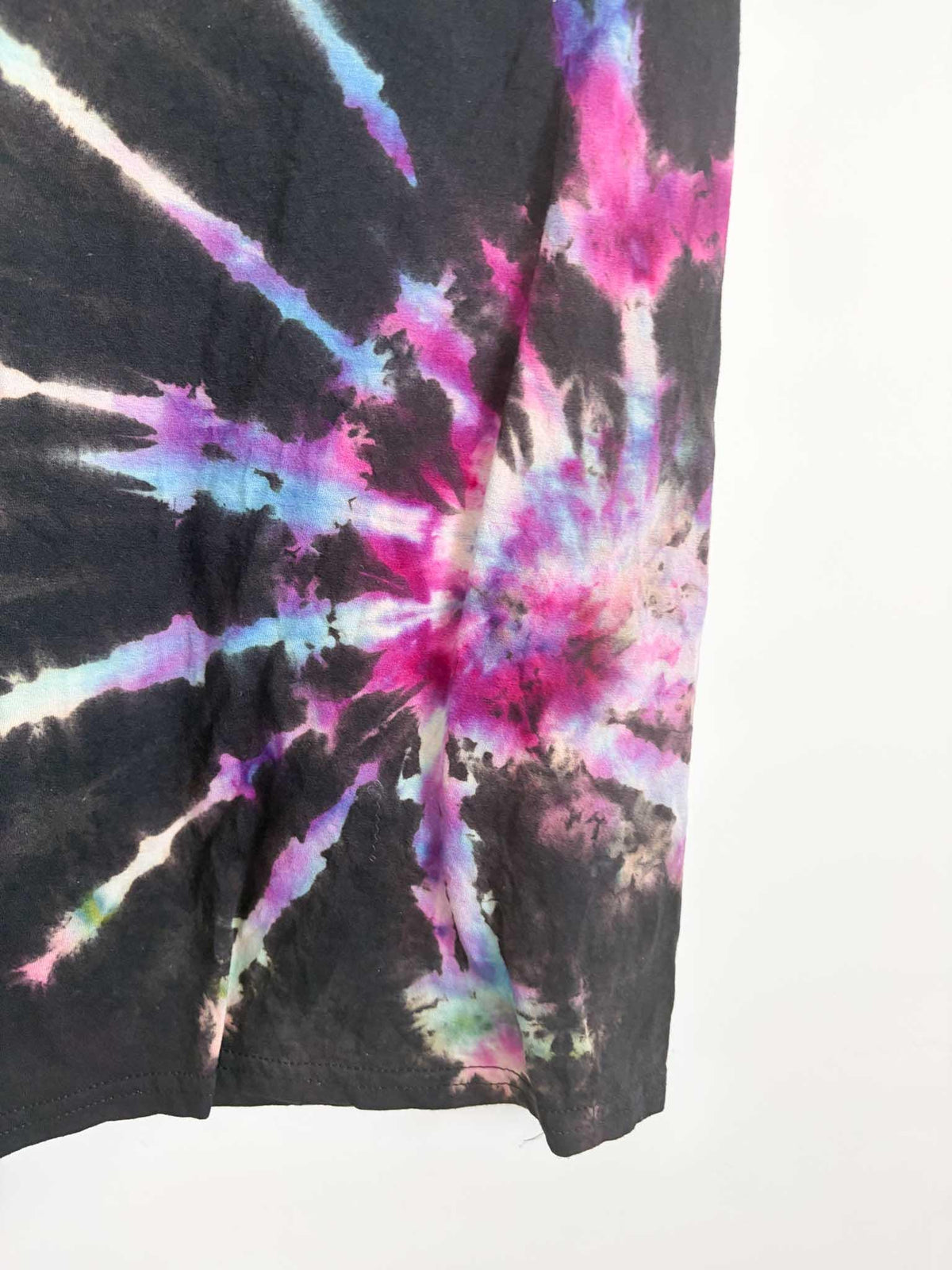Close up detail of pink purple and blue spiral rays on black tie dye t-shirt hem