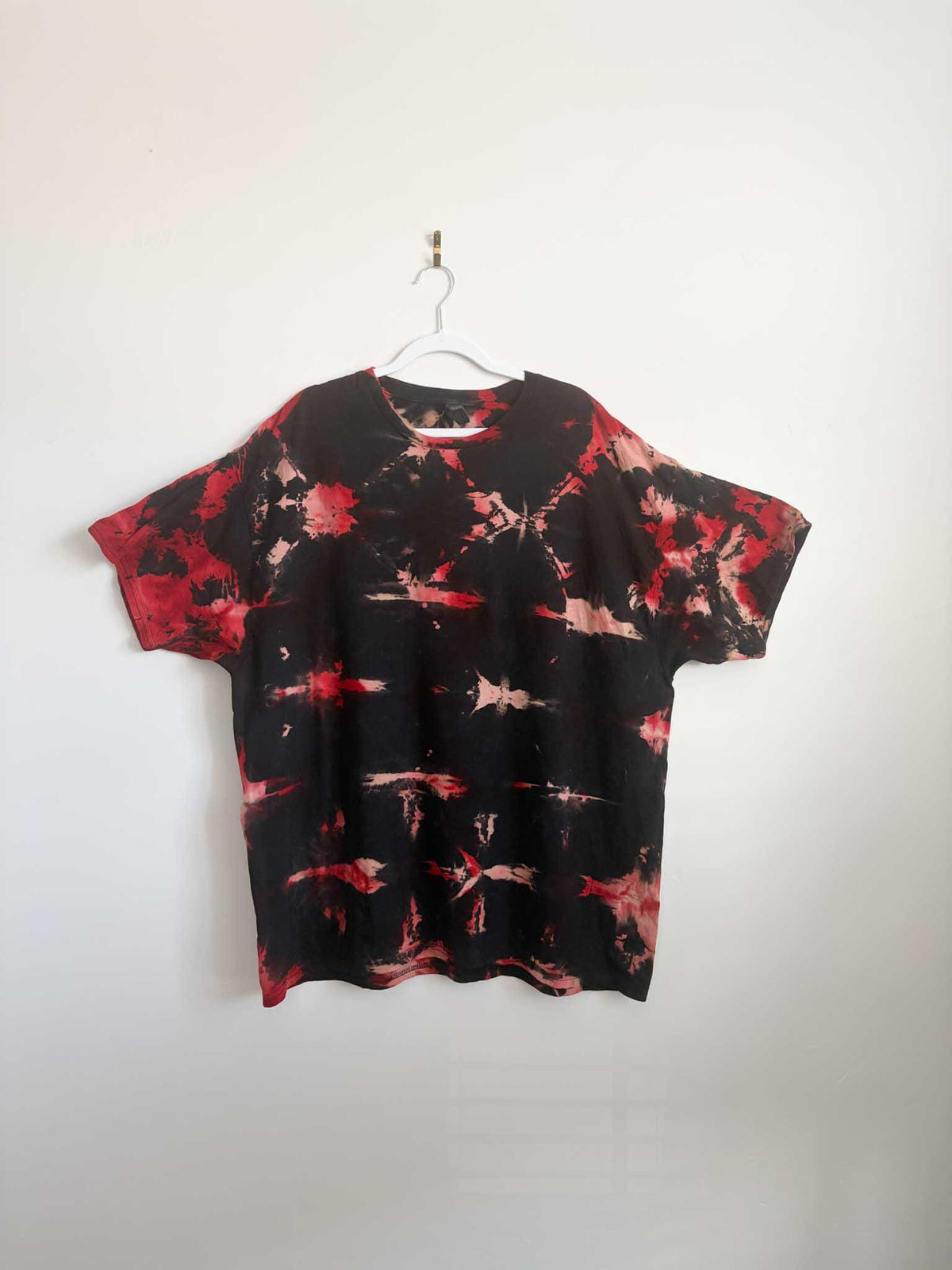 2XL black and red shibori tie dye t-shirt hanging on white hanger against white wall