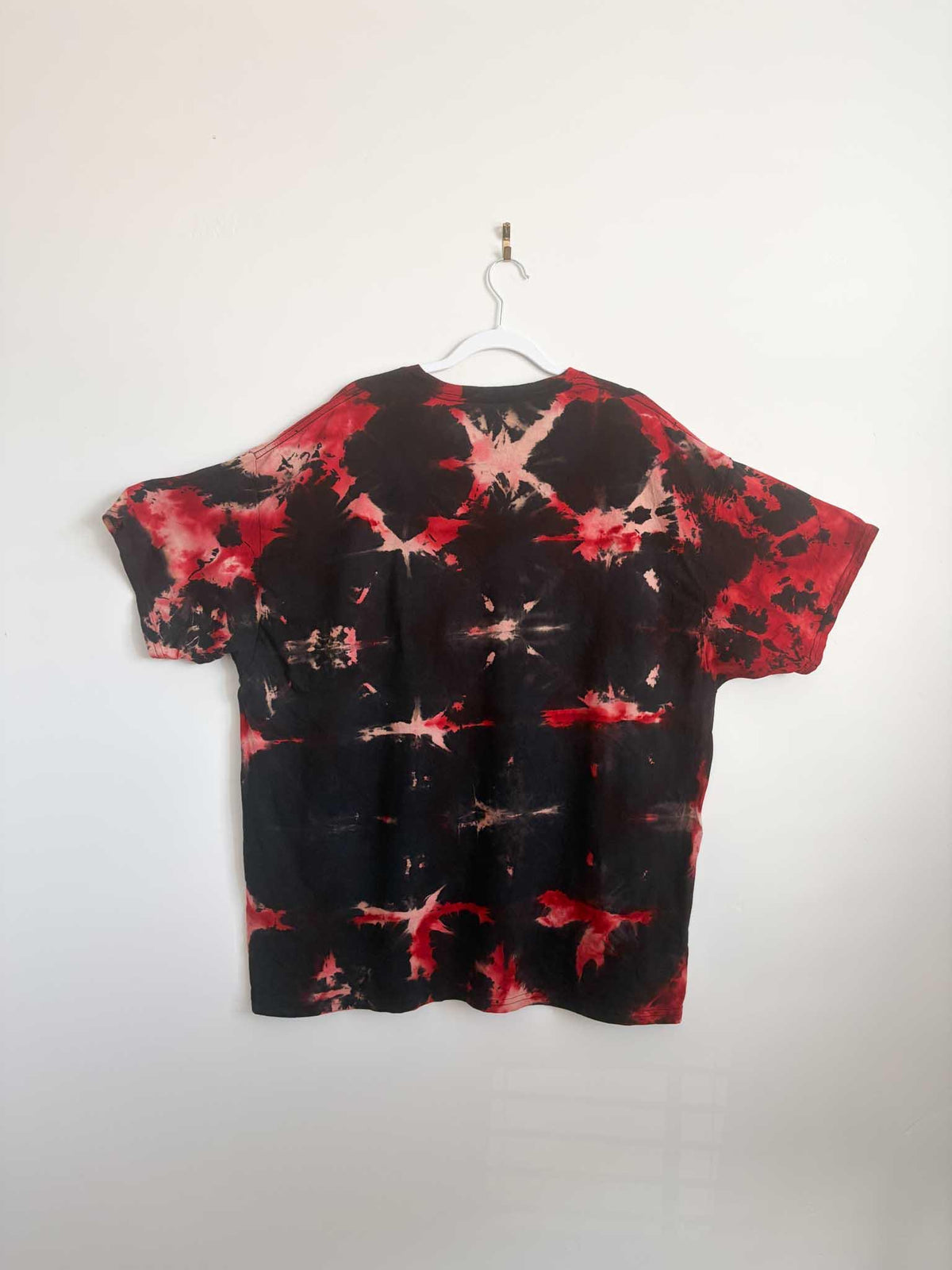 Back view of black and red shibori tie dye t-shirt hanging on white hanger