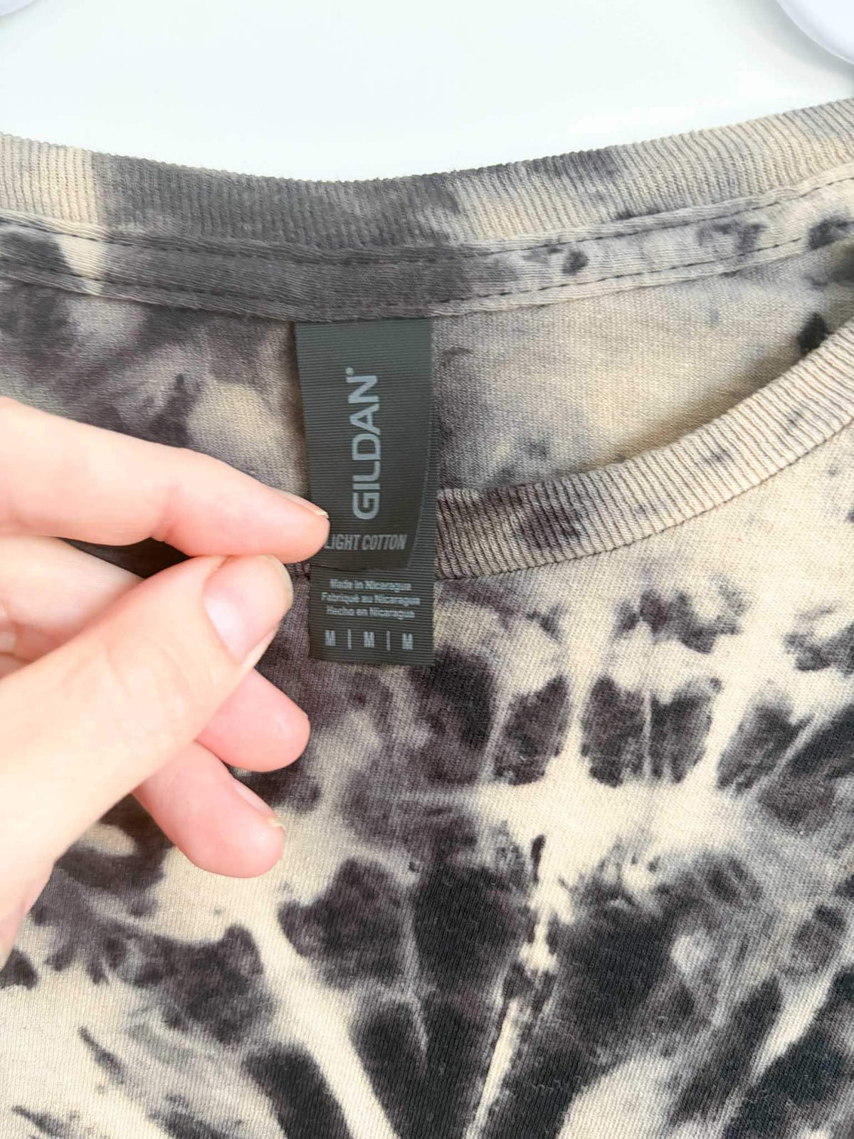 Close up of Gildan Light Cotton size medium tag on tan and black reverse spiral tie dye shirt