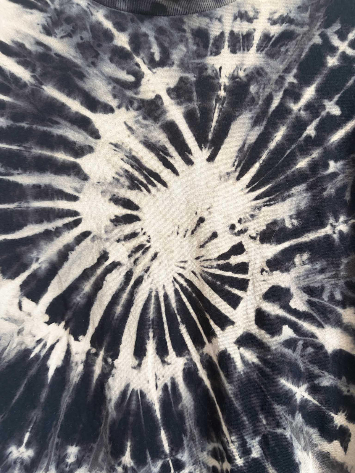 Close up detail of tan and black spiral pattern texture on cotton tie dye t-shirt