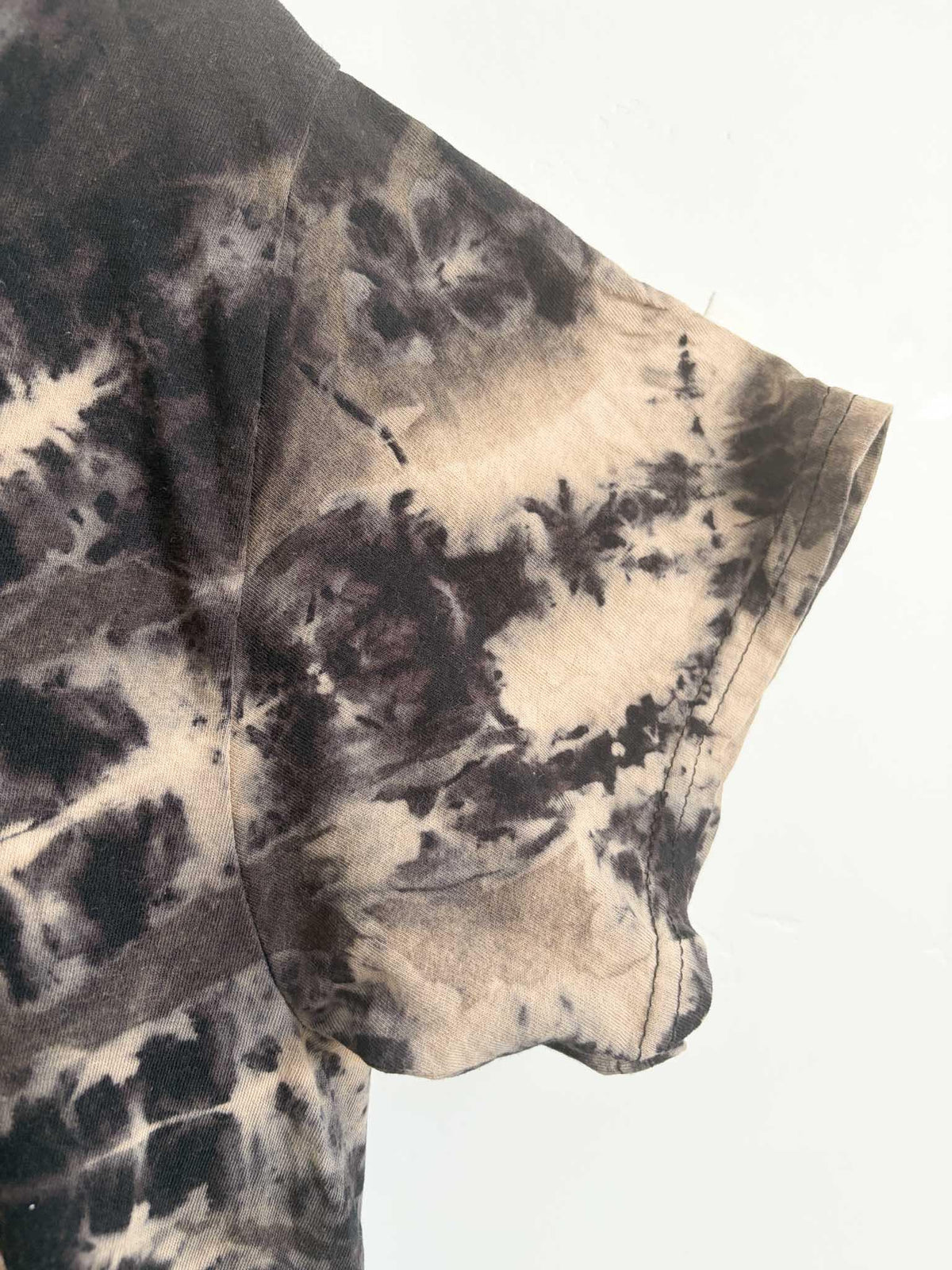 Close up of sleeve and side seam on tan and black reverse spiral bleach tie dye t-shirt