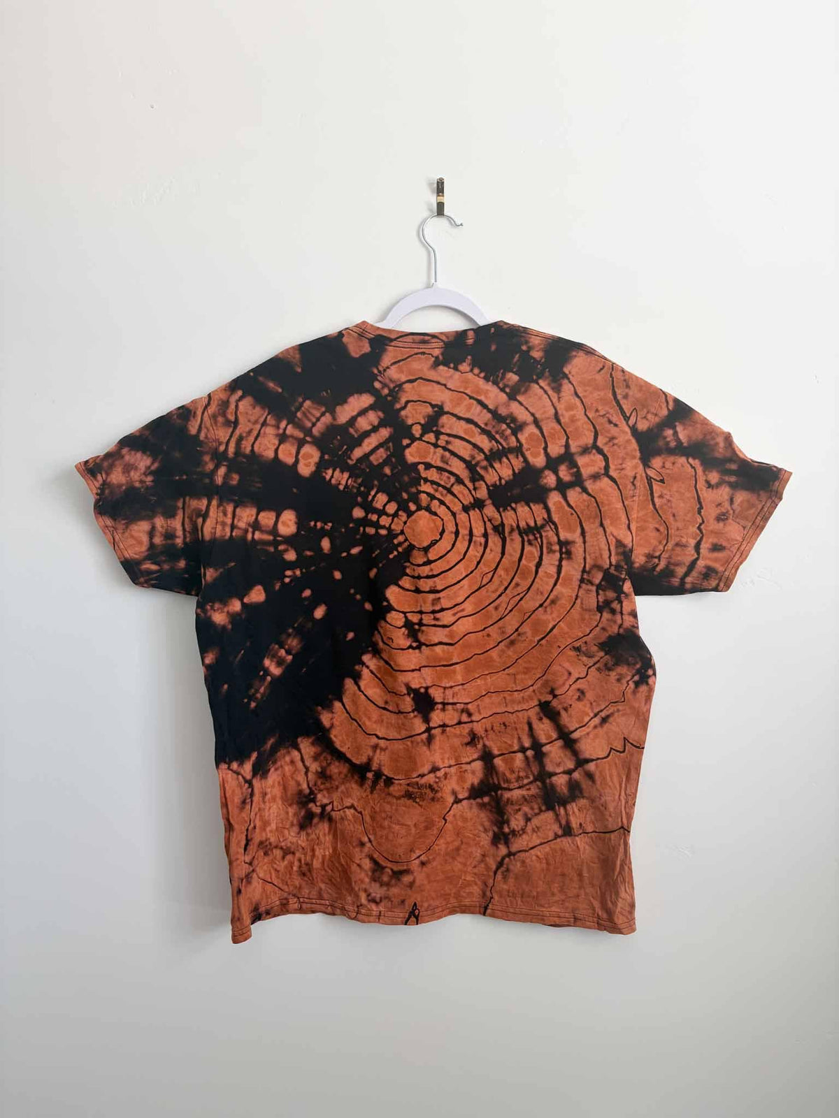 Back view of black shirt with bleached bullseye tie dye pattern in rust and copper tones