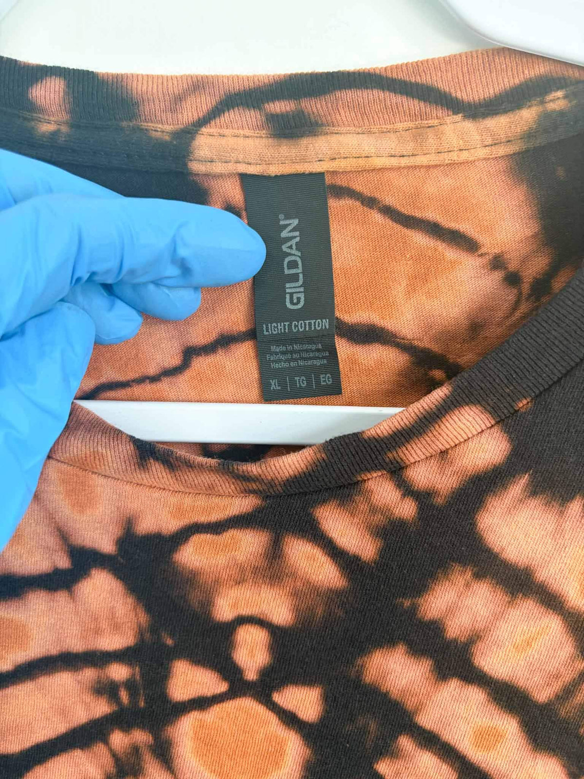 Gildan Light Cotton tag on an XL reverse tie dye bullseye shirt in rust and black