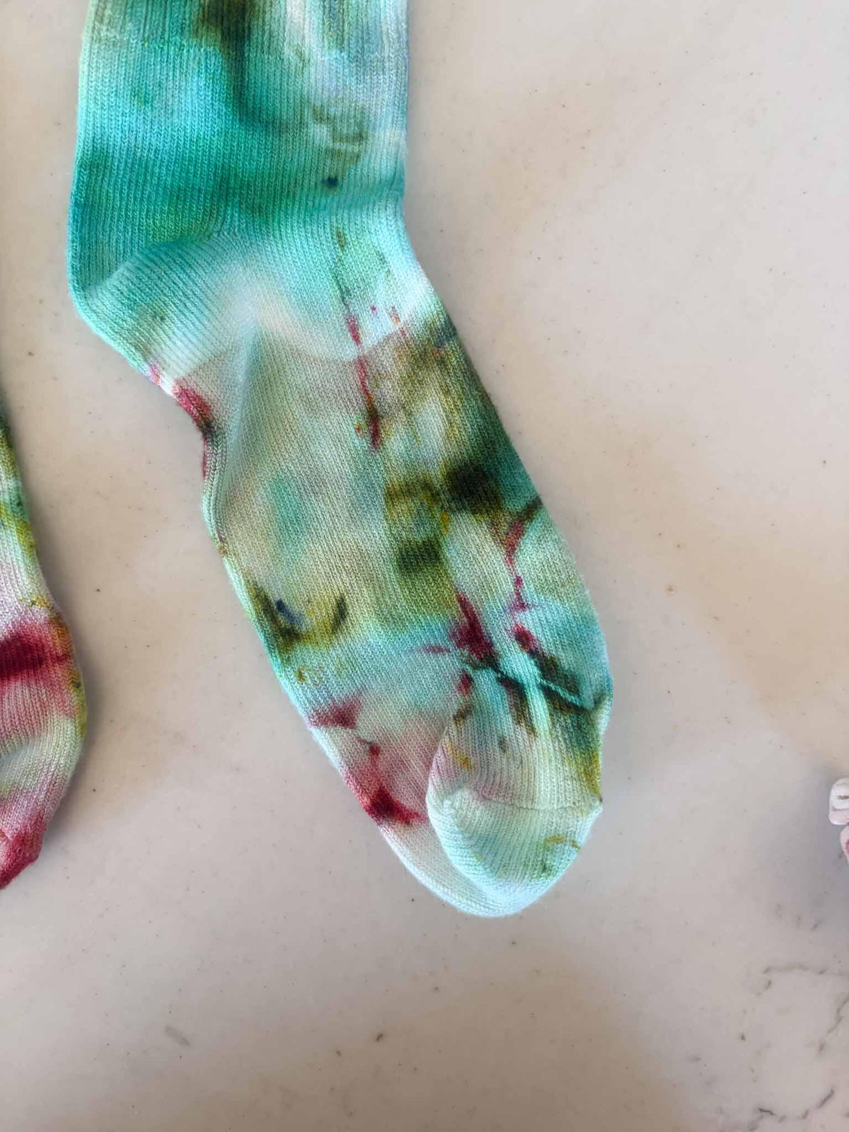 Close-up of sock toe showing green, pink, and gold watercolor tie dye pattern