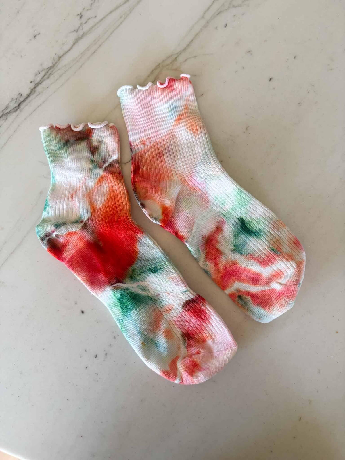 Pair of ruffle cuff ankle socks in coral and seafoam ice dye colorway laid flat