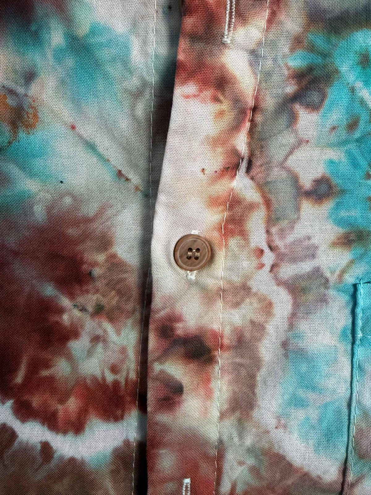 Close up of button placket showing rust, brown, and turquoise ice dye color blending