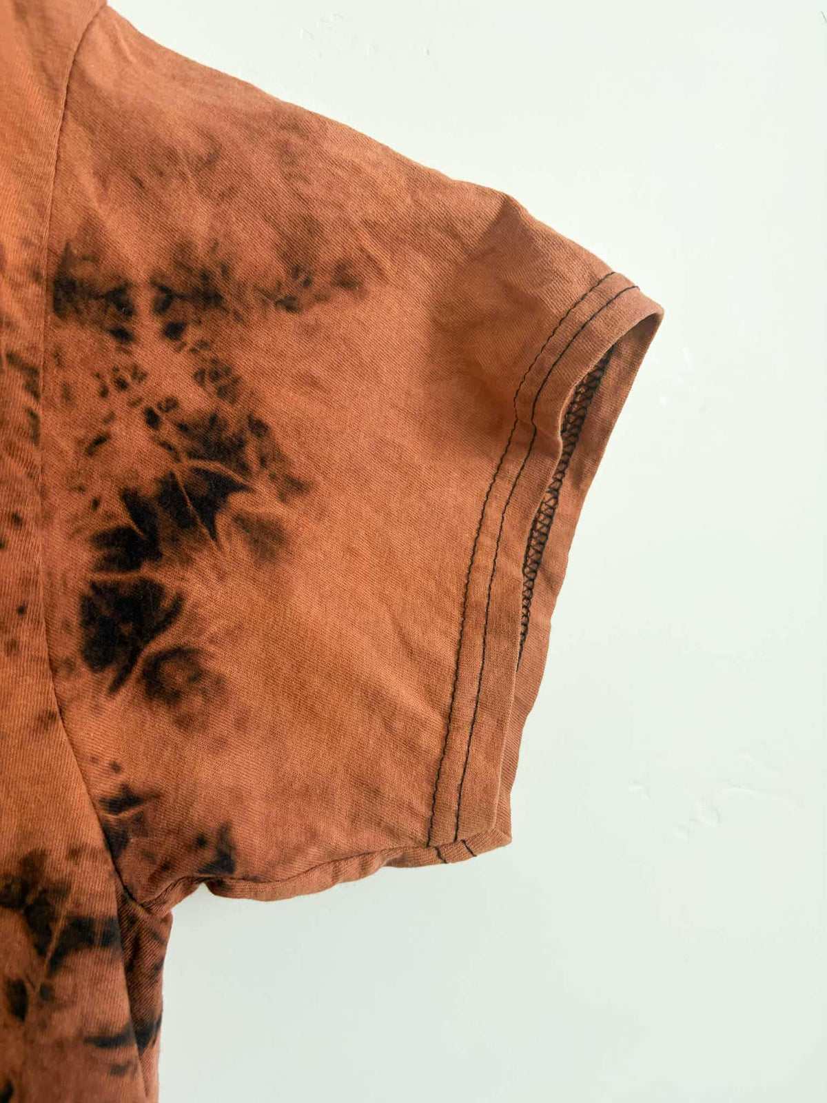 Side view of sleeve and side seam on rust orange and black bleach crumple tie dye t-shirt
