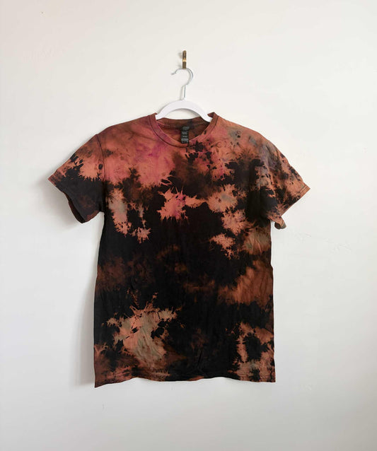Small black rust and pink bleach crumple tie dye t-shirt hanging on white hanger against white wall