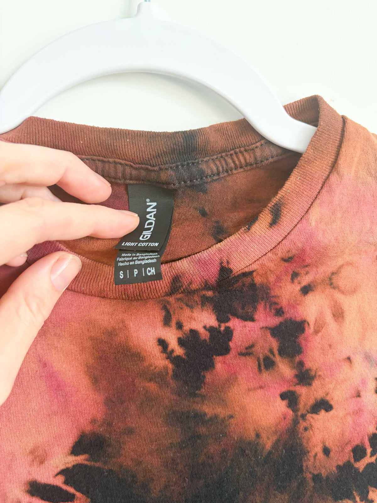 Close up of Gildan Light Cotton size small tag on black rust and pink bleach crumple tie dye shirt