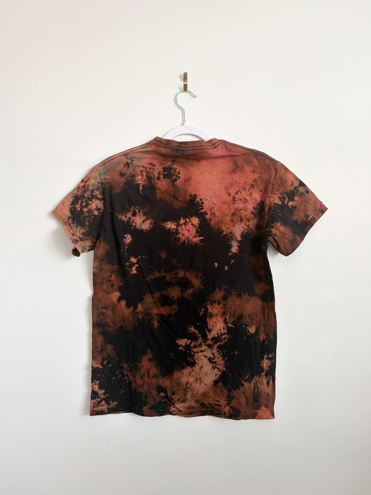 Back view of black rust and pink bleach crumple tie dye t-shirt hanging on white hanger