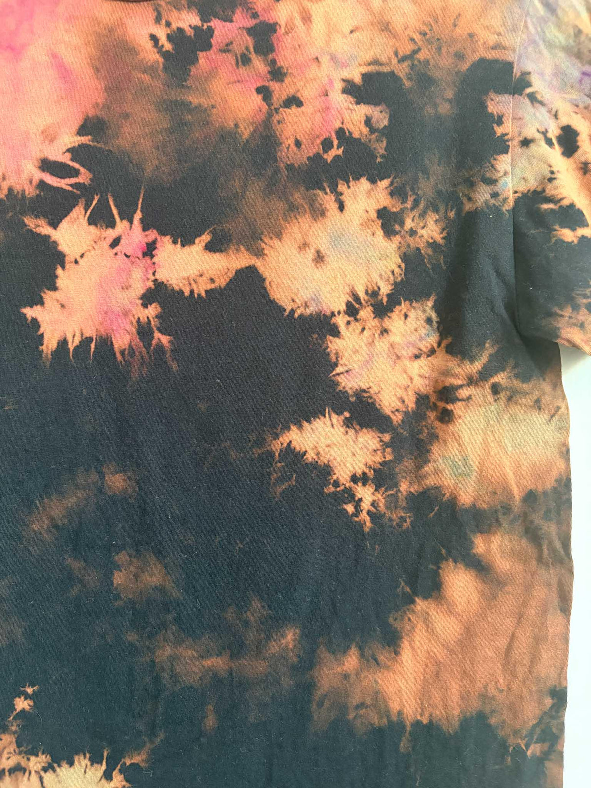 Close up detail of black rust and pink bleach crumple tie dye pattern texture on cotton shirt