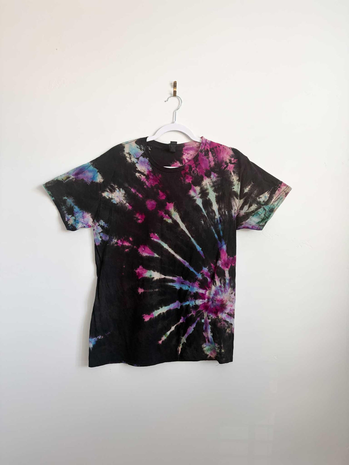 Medium black pink purple and blue galaxy spiral tie dye t-shirt hanging on white hanger against white wall