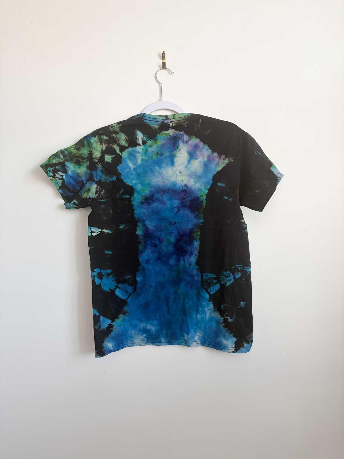Back view of black teal blue and green ice dye mosaic t-shirt hanging on white hanger