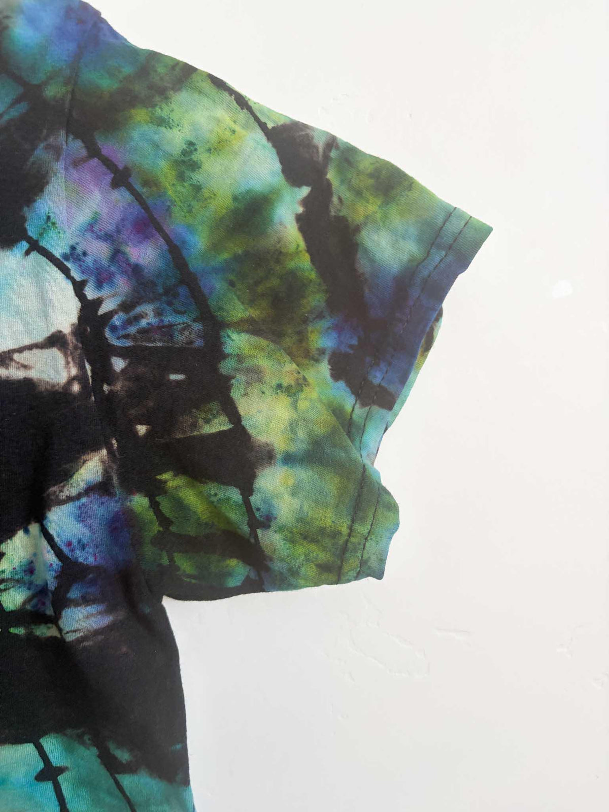 Close up of sleeve and side seam on black teal blue and green ice dye mosaic t-shirt