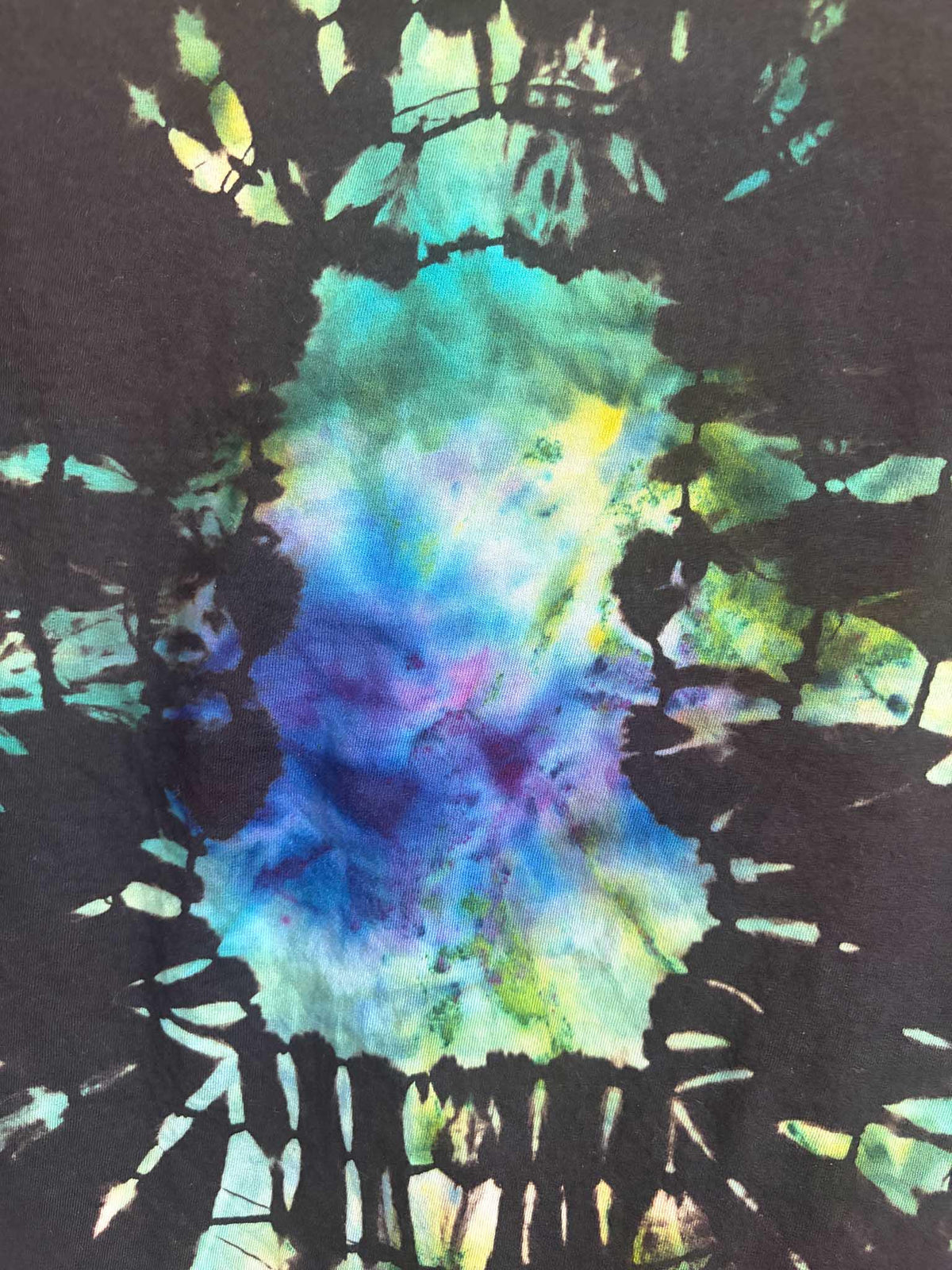 Close up detail of blue purple and green ice dye mosaic pattern texture on black cotton shirt