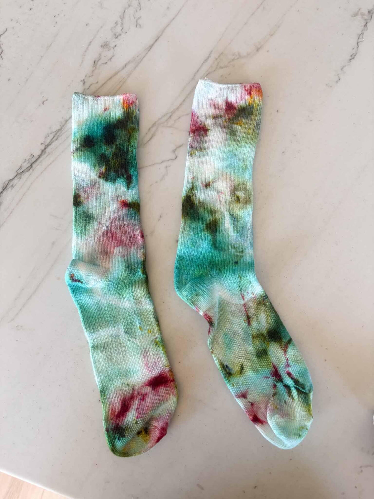 Pair of bamboo crew socks in green and pink ice dye colorway laid flat