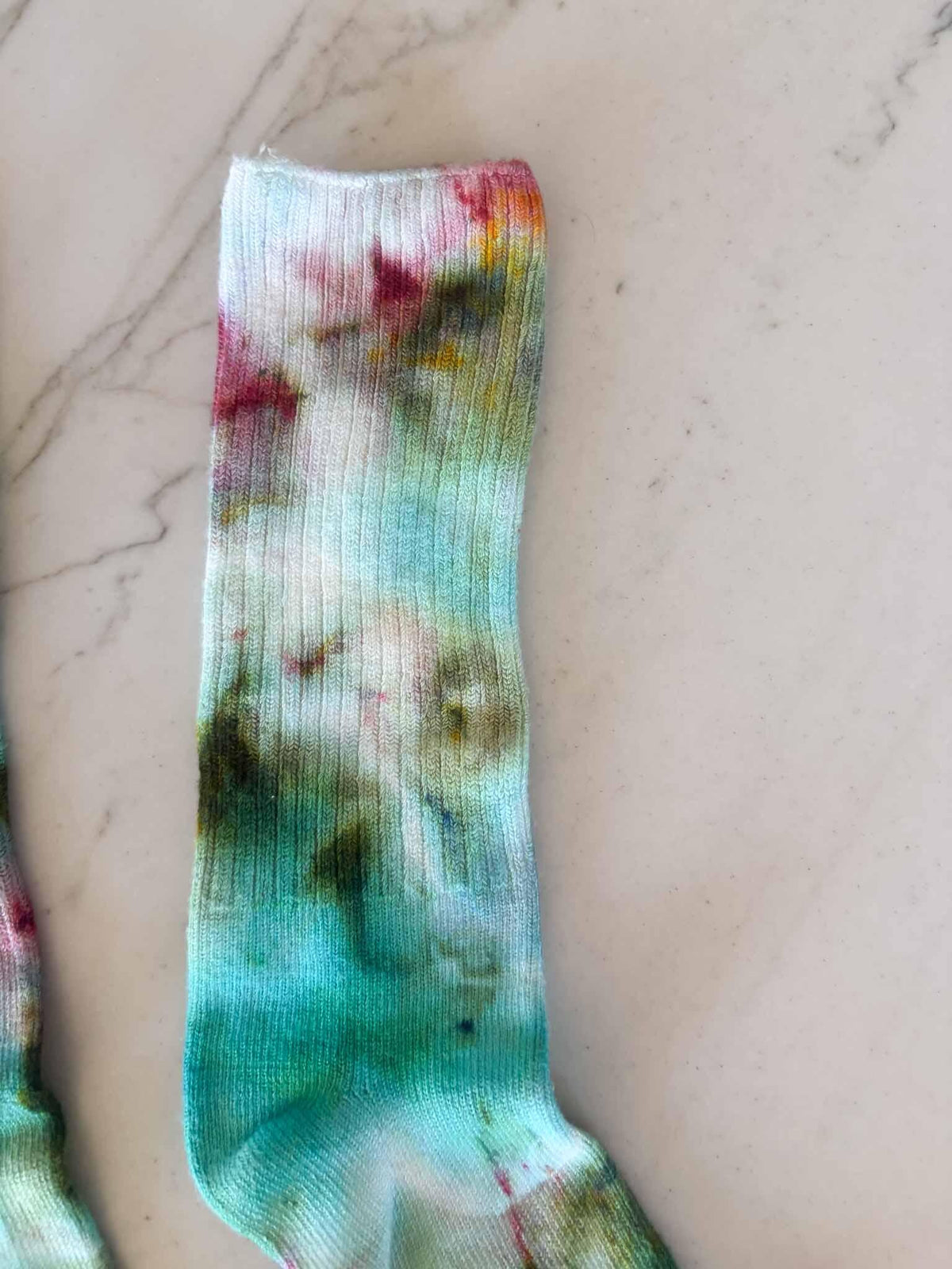 Close-up of sock cuff and leg showing emerald and pink ice dye blend