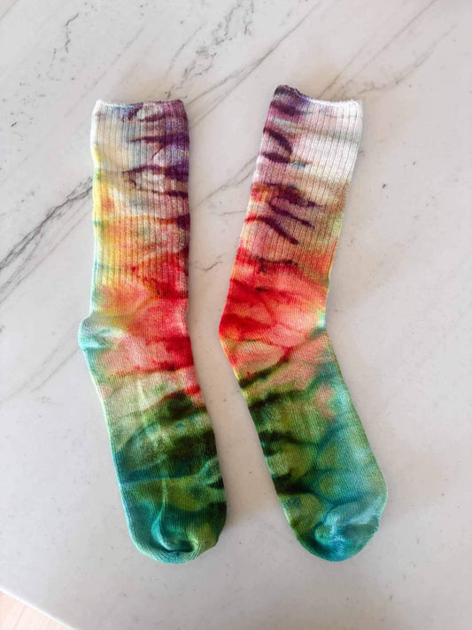 Pair of bamboo crew socks in purple, orange, and green ombre ice dye laid flat