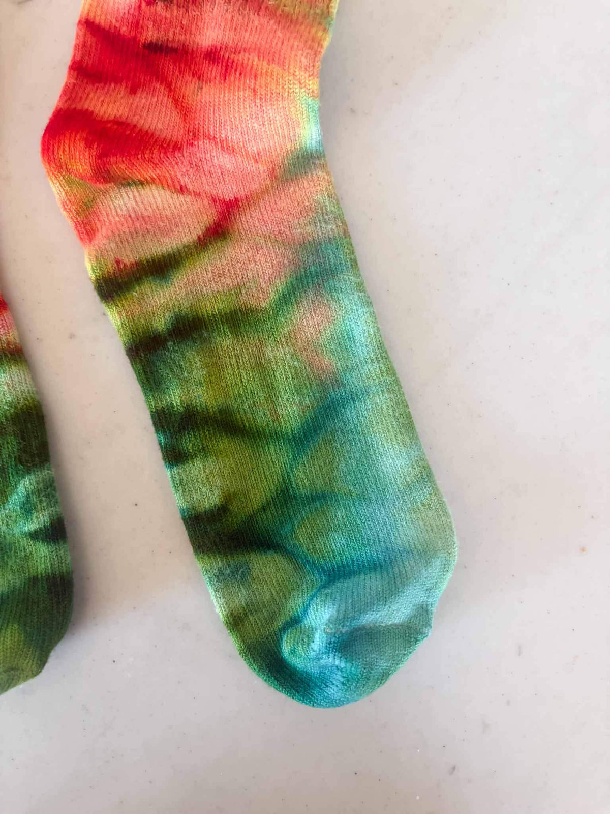 Close-up of sock toe showing red, gold, and green ombre ice dye pattern