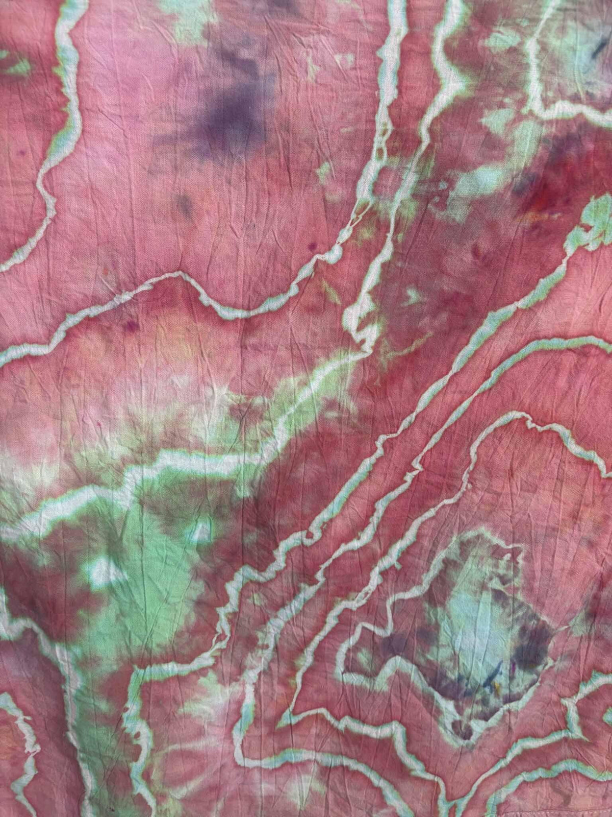 Close-up of ice dyed cotton with jagged white lines edged in mint green winding through raspberry pink dye, with soft purple patches.