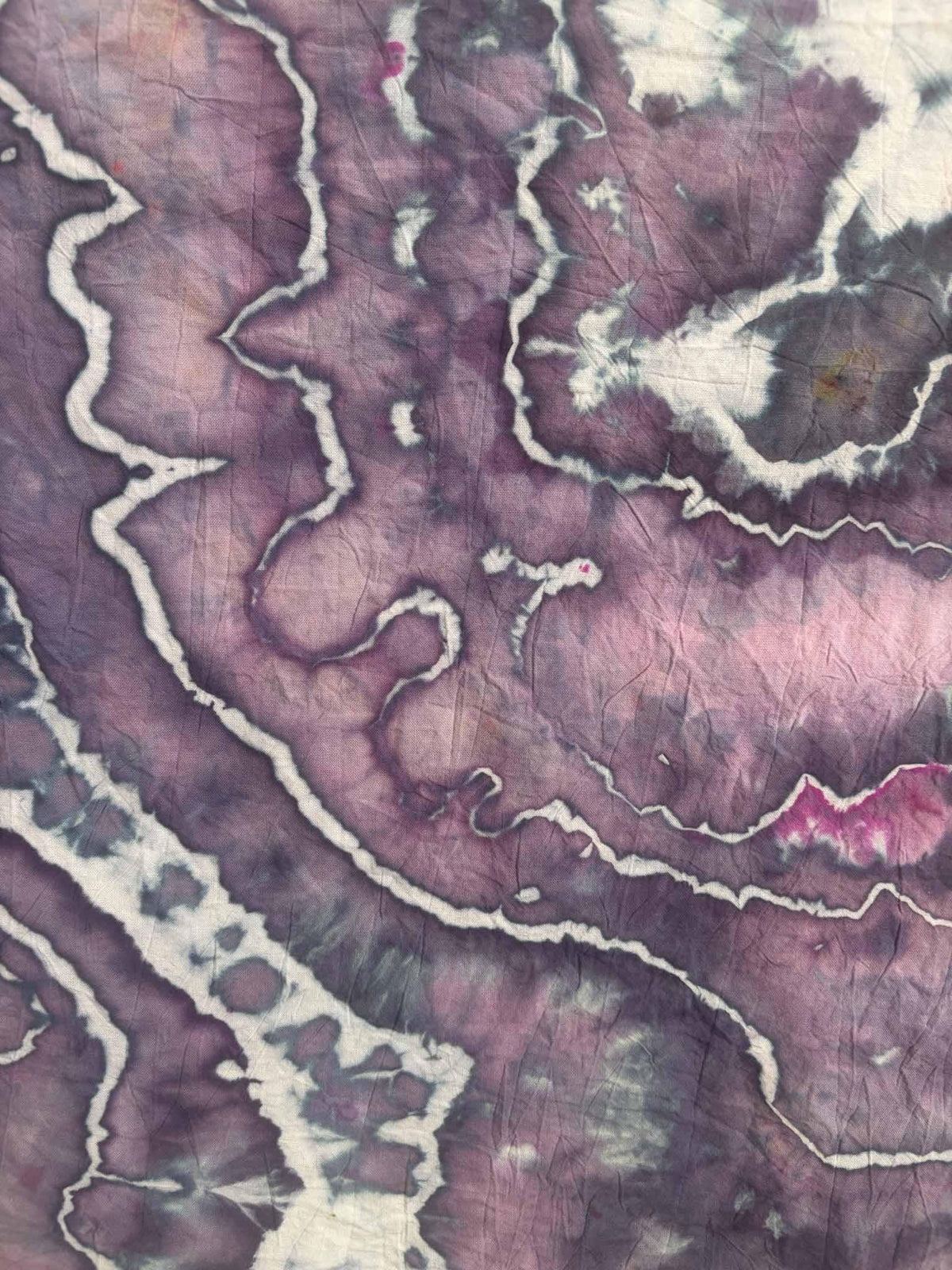 Close-up of ice dyed cotton with zigzag white lines winding through violet and mauve purple dye, with a streak of bright magenta.