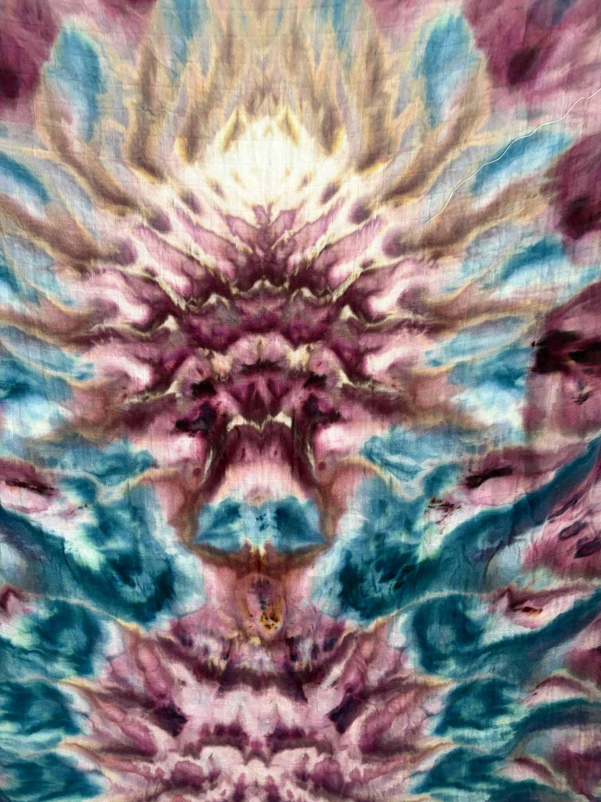Close-up of a symmetrical ice dyed pattern with rays of peach, dusty pink, and cream above mirrored shapes in berry and deep teal.