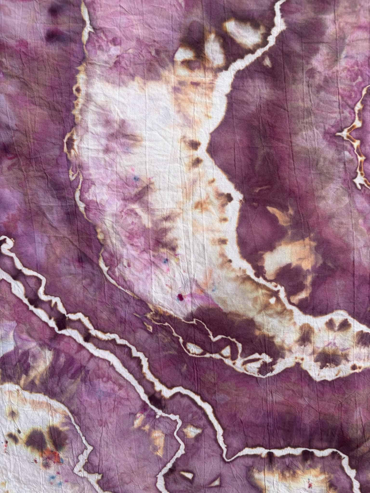 Close-up of ice dyed cotton with a cream white band speckled in chocolate brown and caramel, framed by deep plum purple and jagged white lines.